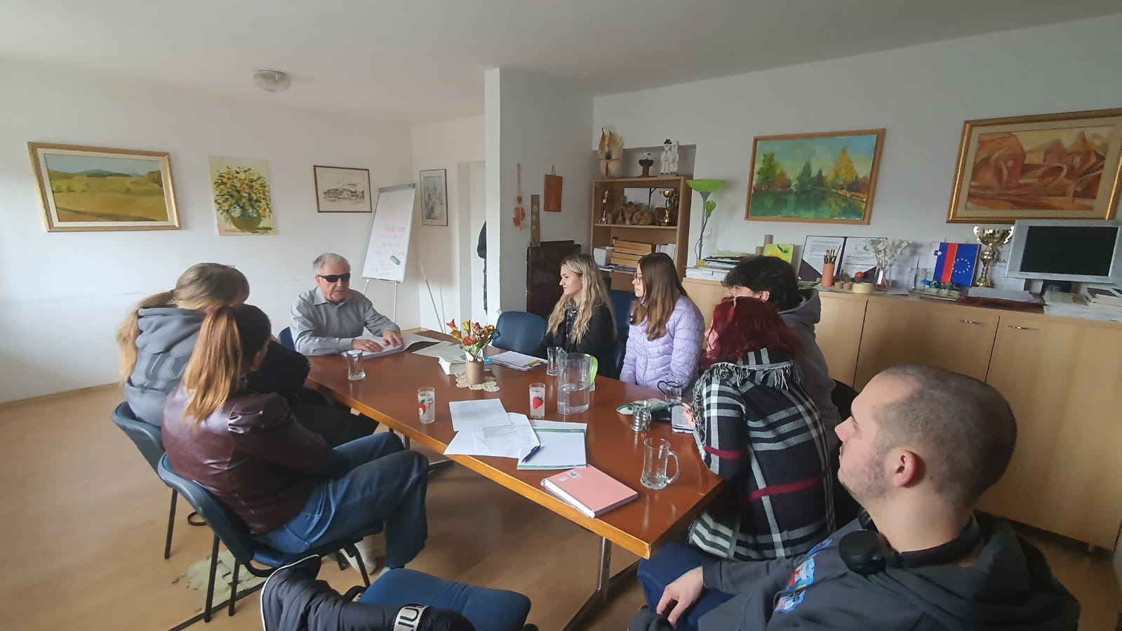 Na fotografiji sedi ekipa Mladinskega centra z gospodom Janezom Kermcem, ki razlaga o potrebah slepih in slabovidnih ter njihovi samostojnosti.